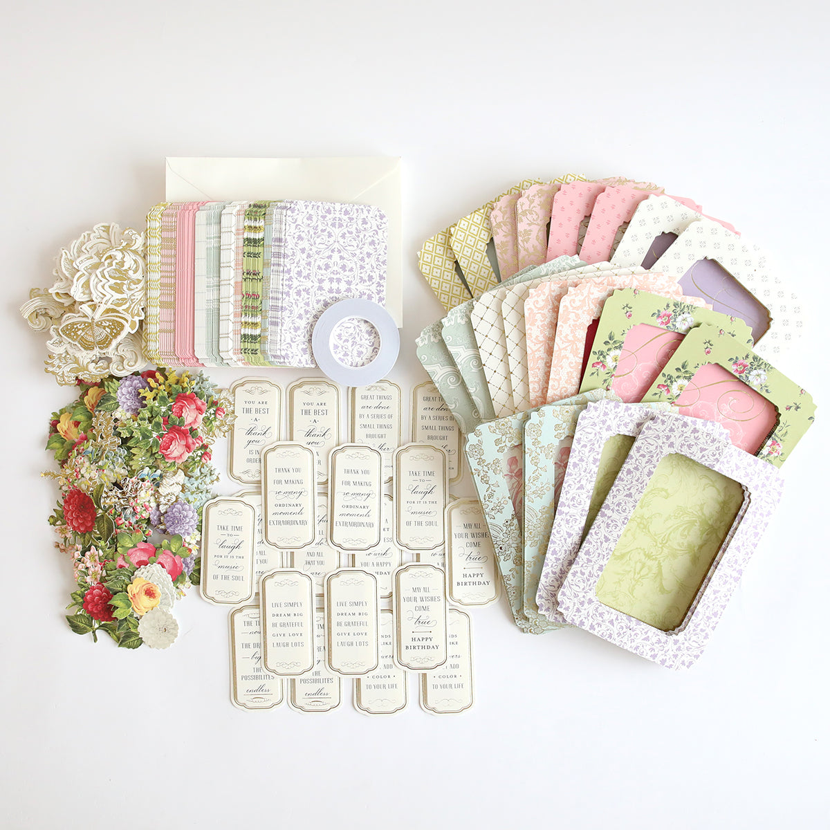 A variety of decorative paper items, such as envelopes, floral cards, die-cut flowers, and frame elements are laid out on a white surface. Ideal for interactive card projects or pairing with the Tunnel Card Making Kit.