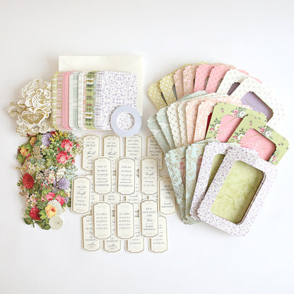 A variety of decorative paper items, such as envelopes, floral cards, die-cut flowers, and frame elements are laid out on a white surface. Ideal for interactive card projects or pairing with the Tunnel Card Making Kit.