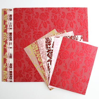 Five sheets of Luxury Tonal Foil Heartfelt Cardstock, embossed with a rose pattern in red, pink, and gold tones, are fanned out on top of a larger coordinating sheet.