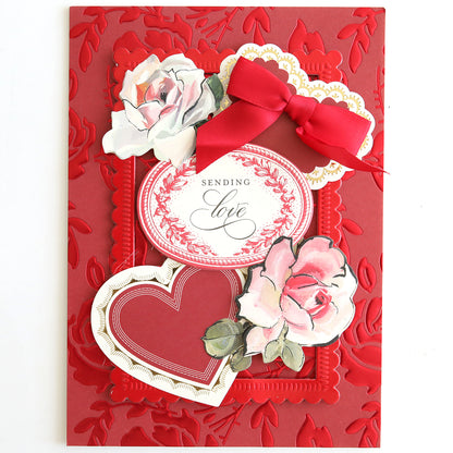A red greeting card on Luxury Tonal Foil Heartfelt Cardstock, featuring embossed florals, two pink roses, a red heart, an ornate "Sending love" label, and a red ribbon bow.