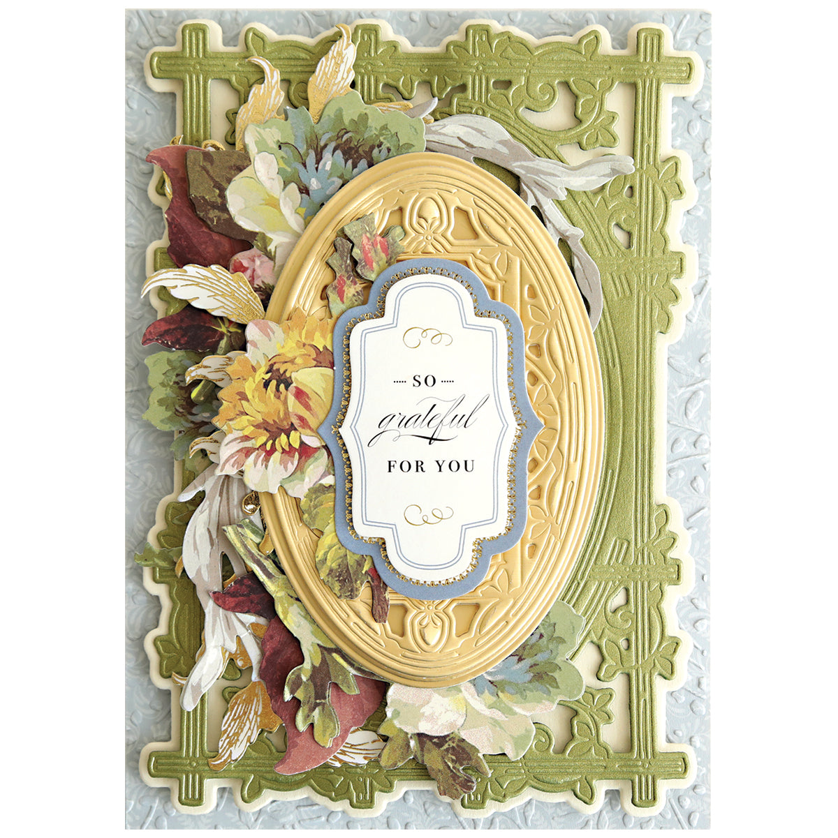A decorative greeting card with layered floral accents, an ornate yellow oval frame made using Woodland 3D Concentric Frame Dies, and a "So Grateful For You" label on a textured green-blue background—ideal for handmade projects.