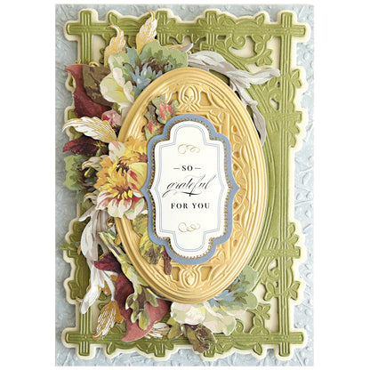 A decorative greeting card with layered floral accents, an ornate yellow oval frame made using Woodland 3D Concentric Frame Dies, and a "So Grateful For You" label on a textured green-blue background—ideal for handmade projects.
