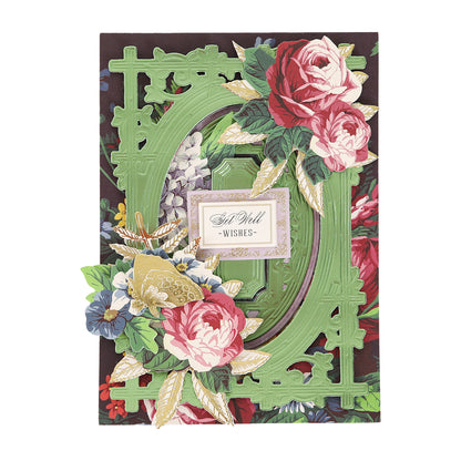 A decorative card, perfect for card making and other handmade projects, features pink and red roses, a green ornate frame created with the Woodland 3D Concentric Frame Dies, and a gold-bordered label that reads “Get Well Wishes” at the center.