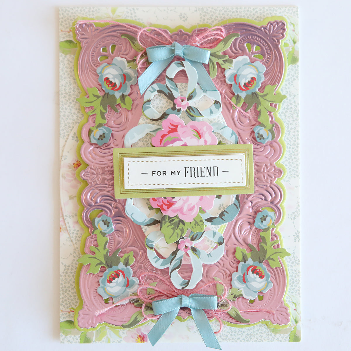 A decorative greeting card featuring Phoebe Die Cut Embellishments, floral designs, pink and blue ribbons, scrapbook accents, and a central label that reads "For My Friend," accented with die cut stickers.
