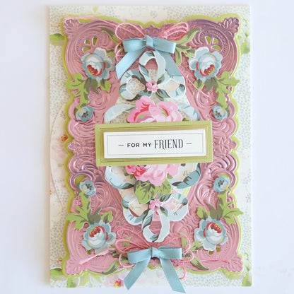 A decorative greeting card featuring Phoebe Die Cut Embellishments, floral designs, pink and blue ribbons, scrapbook accents, and a central label that reads "For My Friend," accented with die cut stickers.