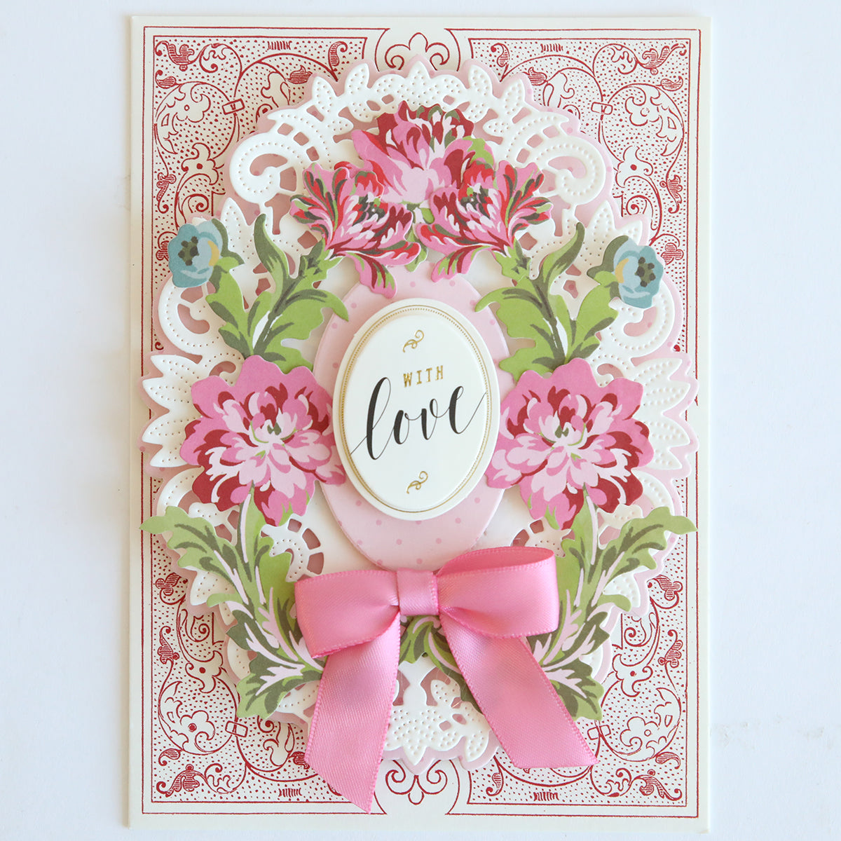 A decorative die cut from the Phoebe Die Cut Embellishments features pink flowers, green leaves, a pink bow, and an ornate border with an oval label reading "With love"—ideal for scrapbook projects.