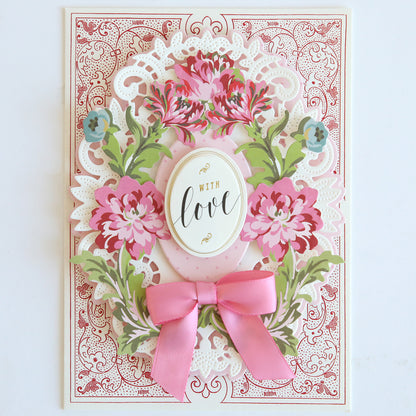 A decorative die cut from the Phoebe Die Cut Embellishments features pink flowers, green leaves, a pink bow, and an ornate border with an oval label reading "With love"—ideal for scrapbook projects.