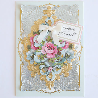 The Phoebe Die Cut Embellishments feature an ornate gold and silver embossed card with pink and blue flowers, a white ribbon, and a "Wishing you well" tag—ideal for scrapbook projects.