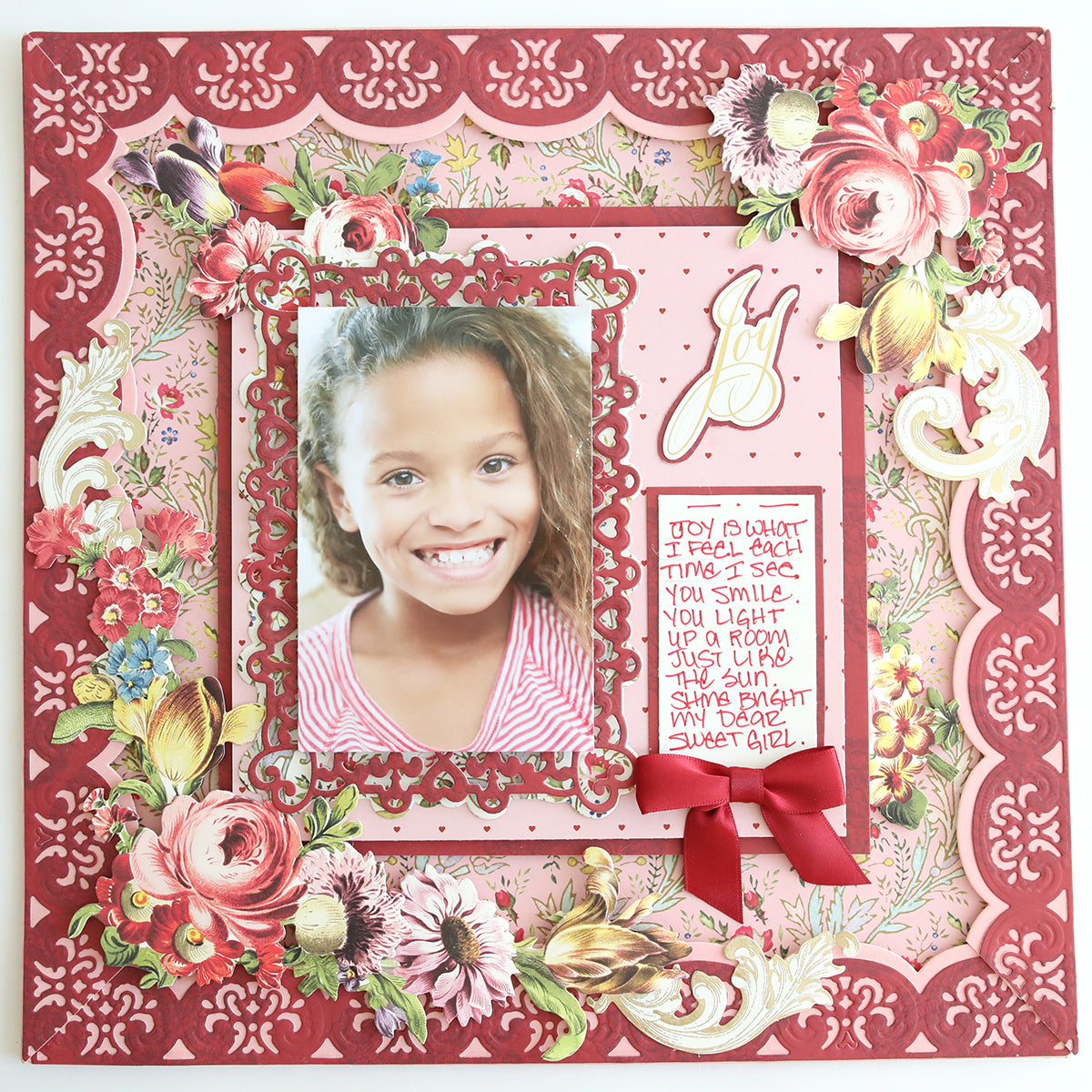 A scrapbook page made with Heartfelt Cardstock and a floral border, featuring a smiling girl in the center, a handwritten note on the right, and a red ribbon bow below the note.