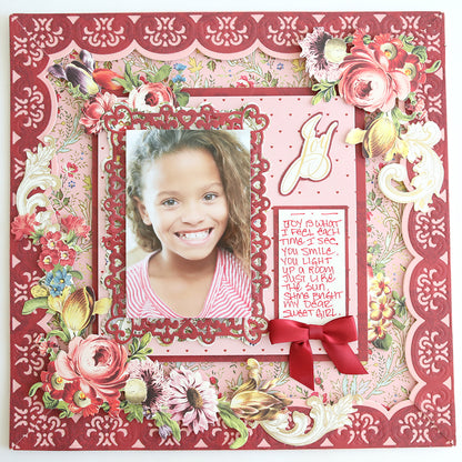 A scrapbook page made with Heartfelt Cardstock and a floral border, featuring a smiling girl in the center, a handwritten note on the right, and a red ribbon bow below the note.