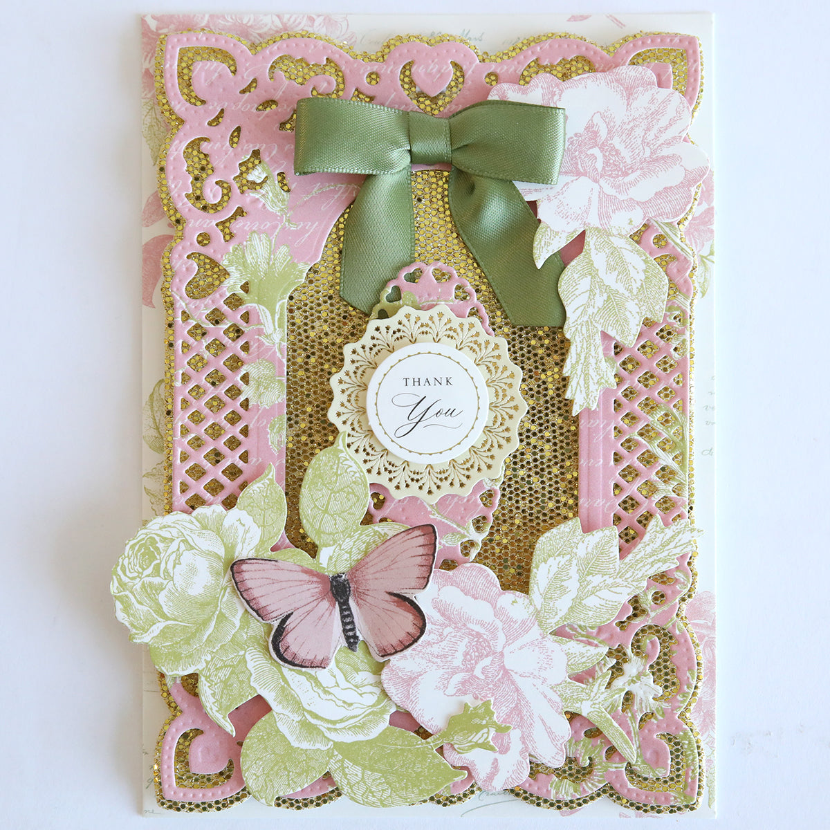 Enhance your Diamond Glitter 12x12 Cardstock with this decorative thank you card featuring pink and gold lace patterns, a green bow, floral accents, and a pink butterfly near the central "Thank You" message. Perfect for scrapbooking!.
