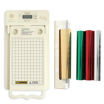 The Empress Gild hot Foil Machine with Holiday Hot Foil, featuring a digital display, grid platform, roll holder, and three foil rolls in gold, red, and green, is displayed on a white background.