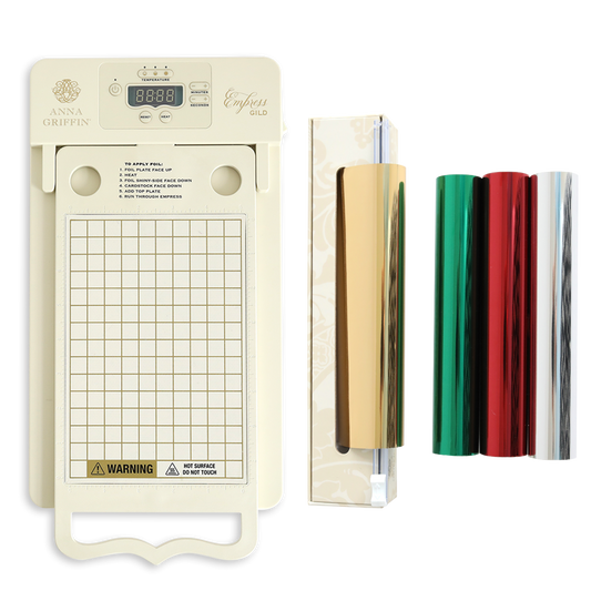 The Empress Gild hot Foil Machine with Holiday Hot Foil, featuring a digital display, grid platform, roll holder, and three foil rolls in gold, red, and green, is displayed on a white background.