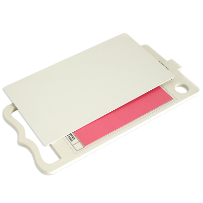 A white cutting board with a handle, partially covered by a white plastic sheet and showing a pink printed label underneath, is perfect for use with the Empress Gild Hot Foil Machine and its heat-activated foiling system.