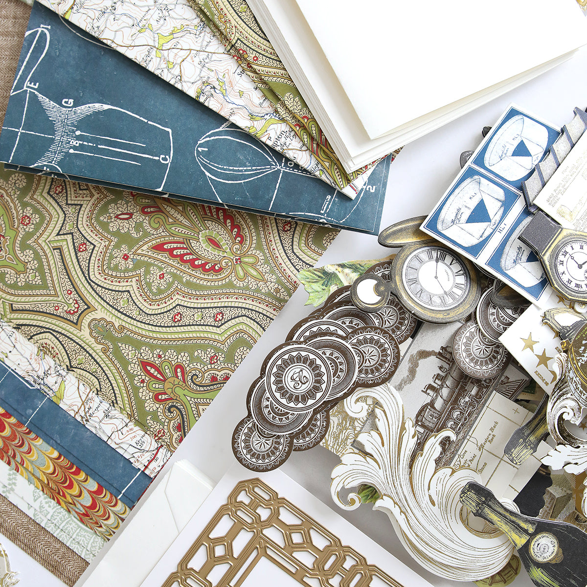 The All About Him Papercrafting Kit with Dies, featuring patterned papers, vintage die cuts, maps, and clock illustrations, is beautifully arranged on a white surface.