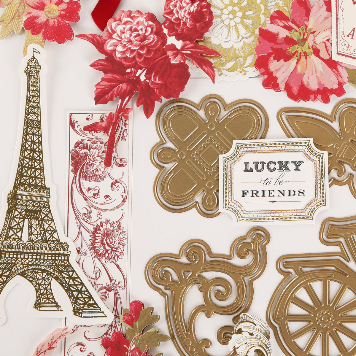 Assorted die-cut embellishments crafted with the Fleur Rouge Papercrafting Kit with Dies—including the Eiffel Tower, gold flourishes, red flowers, and a “Lucky to be Friends” label—arranged on a white background for vintage-inspired papercrafting projects.