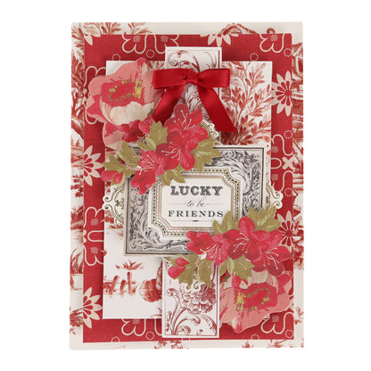 A decorative card featuring red floral patterns, a red bow, and the sentiment “Lucky to be Friends” at the center surrounded by red and green flowers, beautifully crafted with the Fleur Rouge Papercrafting Kit with Dies for a touch of vintage-inspired papercrafting charm.