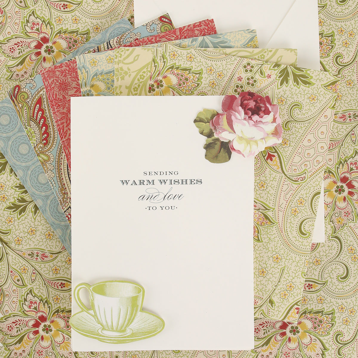 A vintage greeting card created with the Haven Papercrafting Kit with Dies, featuring “Sending warm wishes and love to you” text, a die-cut floral embellishment, a teacup, and patterned paper envelopes.