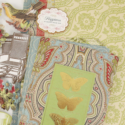 The Haven Papercrafting Kit with Dies features paisley and floral prints, layered with die-cut images of a bird, a rocking chair, and flowers, alongside a butterfly card reading “Happiness is being near you.”