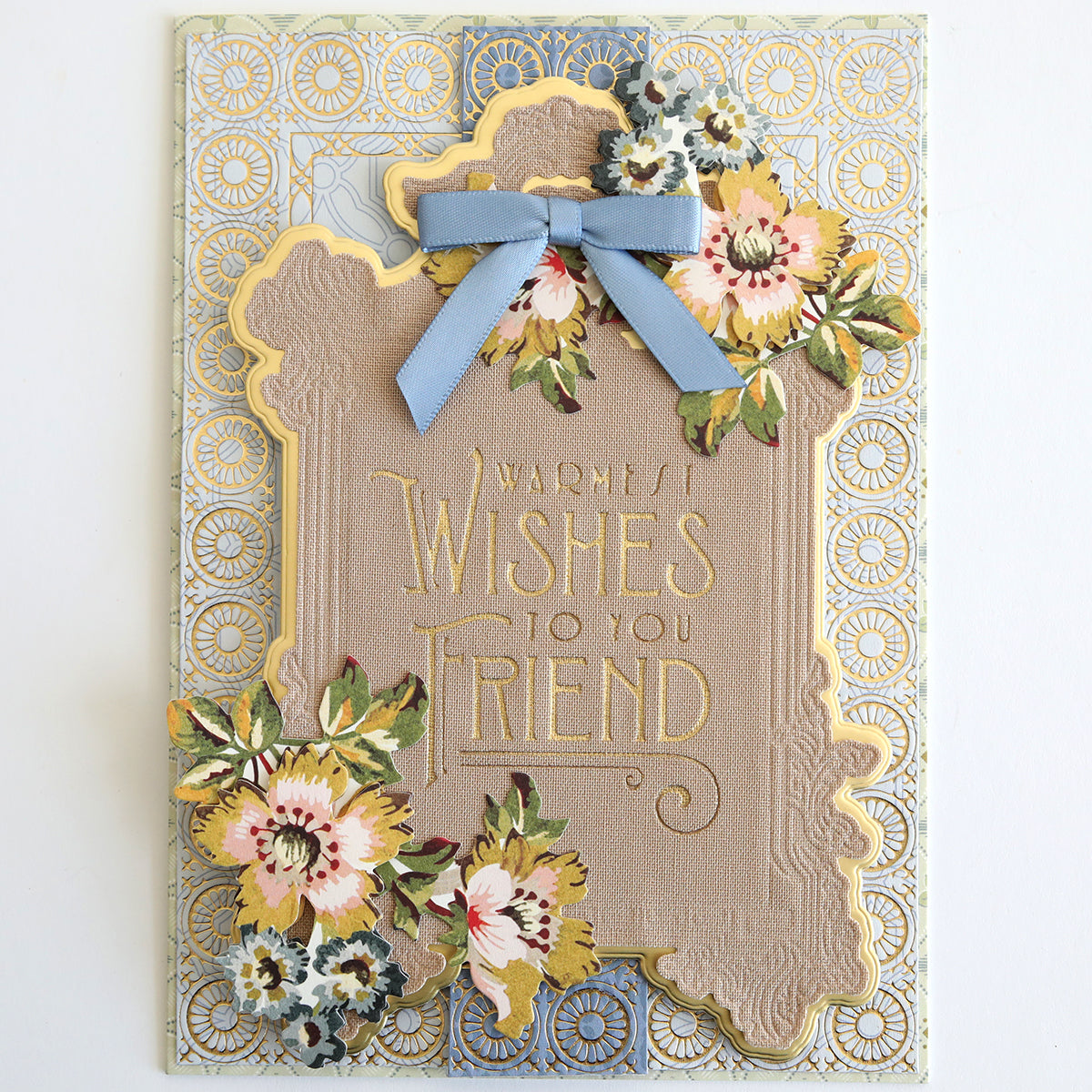 The Fabric Card Layers Neutral features a handmade decorative card with gold and pastel florals, a blue bow, and "Warmest Wishes To You Friend" embossed in the center, crafted with elegant neutral fabric cardstock layers.