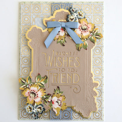 The Fabric Card Layers Neutral features a handmade decorative card with gold and pastel florals, a blue bow, and "Warmest Wishes To You Friend" embossed in the center, crafted with elegant neutral fabric cardstock layers.