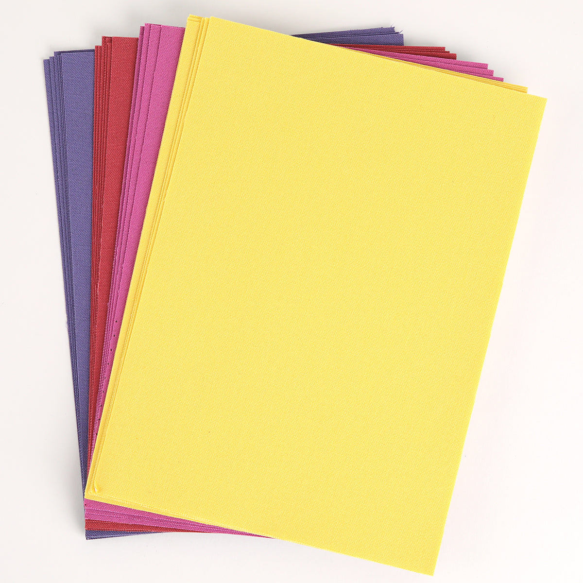 A stack of rectangular Bright Fabric Card Layers in yellow, purple, pink, and red is arranged on a white background—perfect for scrapbooking or card making.