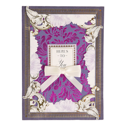 Introducing Bright Fabric Card Layers: a decorative greeting card featuring fabric layers with vibrant purple floral patterns, elegant gold accents, a charming white bow, and the heartfelt message “HERE’S TO You” in the center—perfect for scrapbooking or card making enthusiasts.