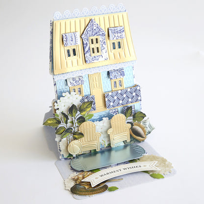 A 3D pop-up card features a house with Adirondack chairs, plants, and a “Warmest Wishes” message—perfect for coastal scrapbooking or pairing with Summer House Cardstock and Embellishments.