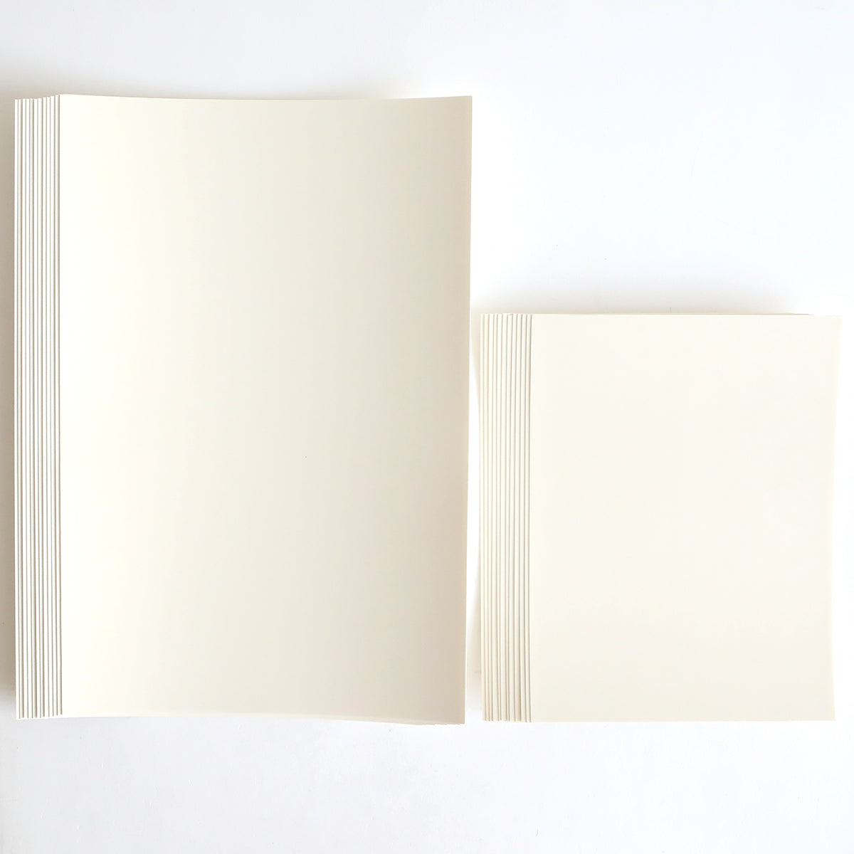 Two stacks of Luxury Ivory Soft Matte 250gsm Cardstock are side by side on a white surface; the left stack is larger than the right.