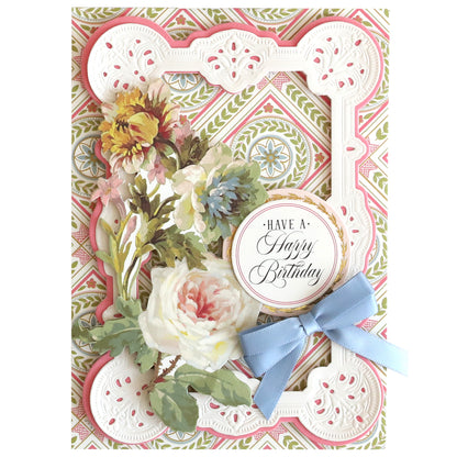 A decorative birthday card with floral designs, ornate white frame, blue ribbon, and “Have a Happy Birthday” label, printed on Luxury Ivory Soft Matte 250gsm Cardstock for an elegant finish.