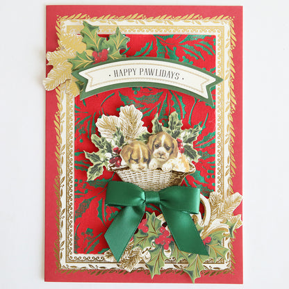 Greeting card with gold and red holiday designs, green ribbon, holly, and a puppy in a basket. Featuring Holiday Fabric Card Layers for festive texture, this card is perfect for Christmas crafting projects. Text reads "Happy Pawlidays.