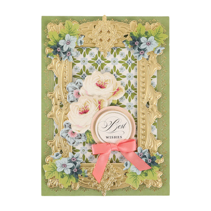 Greeting card featuring Cottage Roses Embellishments with an ornate gold frame, white and pink flowers, blue blossoms, a “Best Wishes” label, and a pink ribbon on a green background—beautifully accented with floral details for added charm.