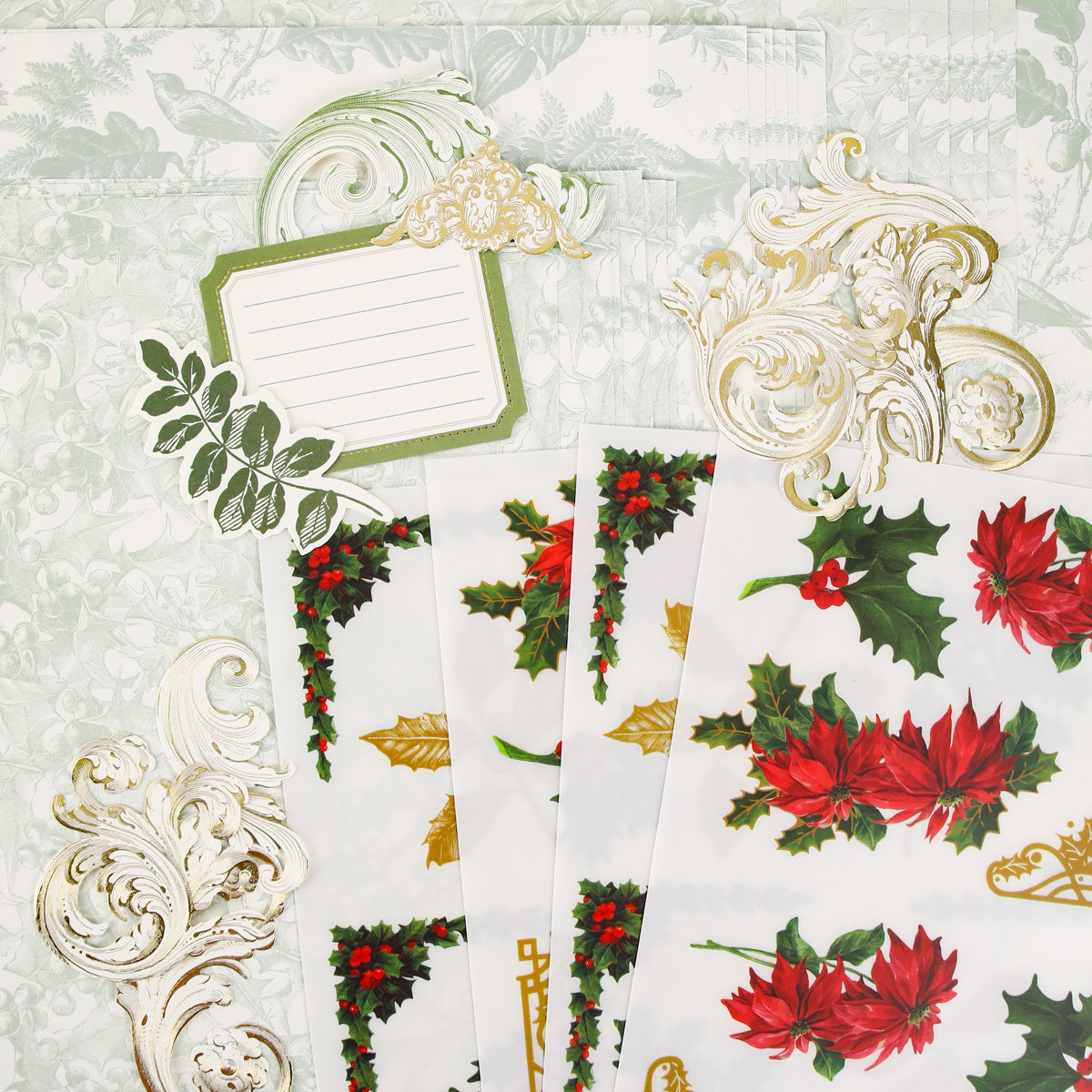 Paper sheets from Anna Griffin | Create Fall 2026, featuring festive floral and holly designs with ornate gold embellishments and a blank label card, are beautifully arranged on a pale green patterned background—ideal inspiration for crafters or upcoming classes as you plan creative projects for the season.