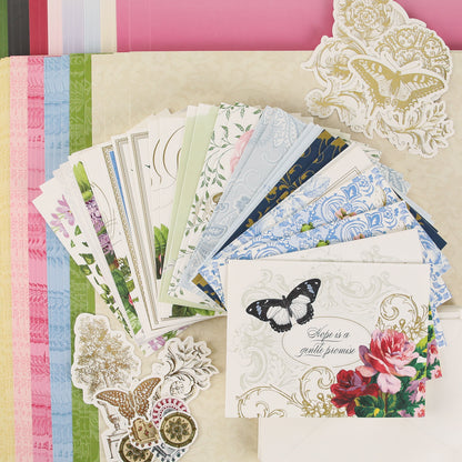 A colorful assortment of patterned papers, floral and butterfly-themed cards, and decorative stickers from Anna Griffin | Create Fall 2026 are arranged on a tabletop, inviting you to join our craft classes and connect with a vibrant creative community as we prepare for the season.