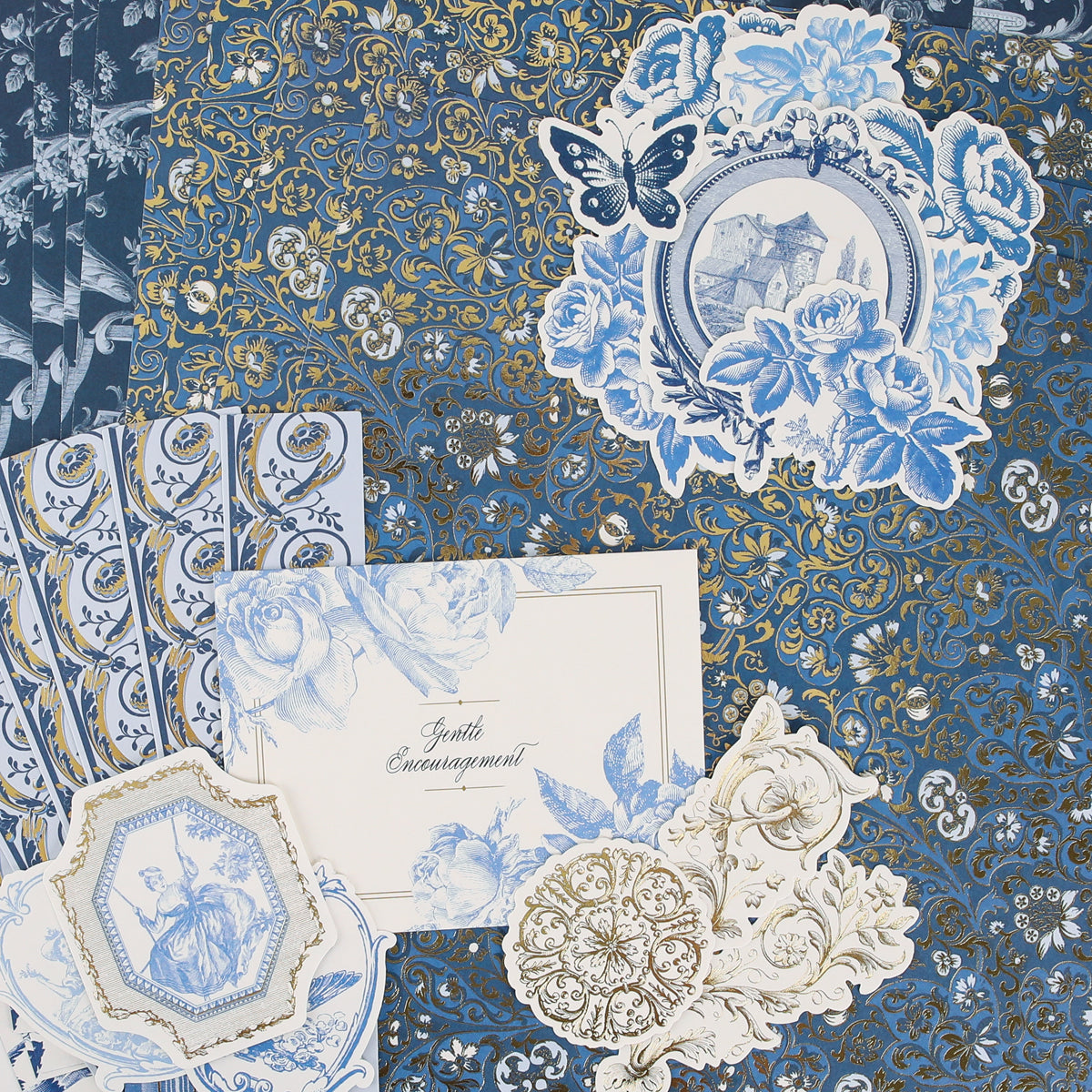 Anna Griffin | Create Fall 2026 features assorted blue and gold decorative papers with floral and butterfly motifs, ornate patterns, and a card reading “Gently Encouragement,” beautifully arranged in a flat lay—ideal inspiration for craft classes or anyone looking to connect with a creative community.