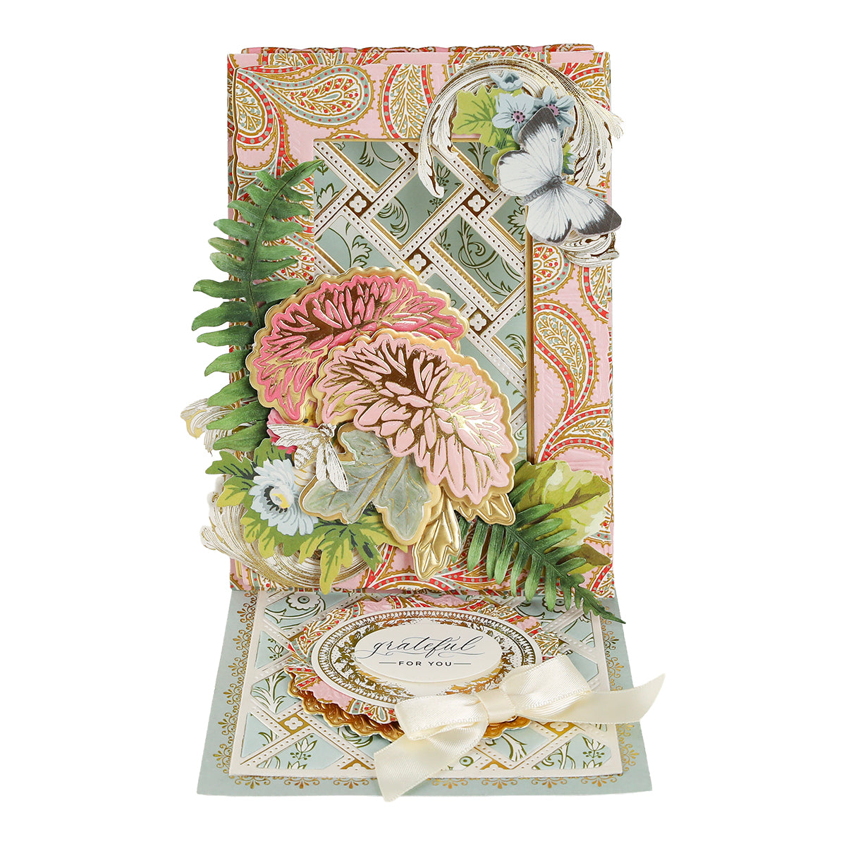 Using the provided product data, here is a rewritten version of your sentence: A handcrafted, decorative card created with the Dahlia, Mum and Sunflower 3D Floral Dies showcases intricate botanical details with floral and fern motifs in soft colors, features embossed accents and a “grateful for you” message, and is displayed upright with a ribbon embellishment.