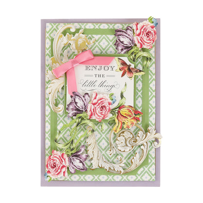 Decked with ornate floral decorations, a pink bow, and the phrase “Enjoy the little things” on a green patterned background adorned with cream, pink, yellow, and purple blooms, this greeting card sparkles thanks to Gold Foil Flourish Stickers. These metallic sticker embellishments lend scrapbook-inspired shine and elegance to your heartfelt message.