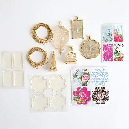 A jewelry kit named "Set of 2 Gold Necklaces Kit," showcasing gold statement necklaces, pendants, wire, and floral-patterned paper cutouts, all elegantly displayed on a white background.