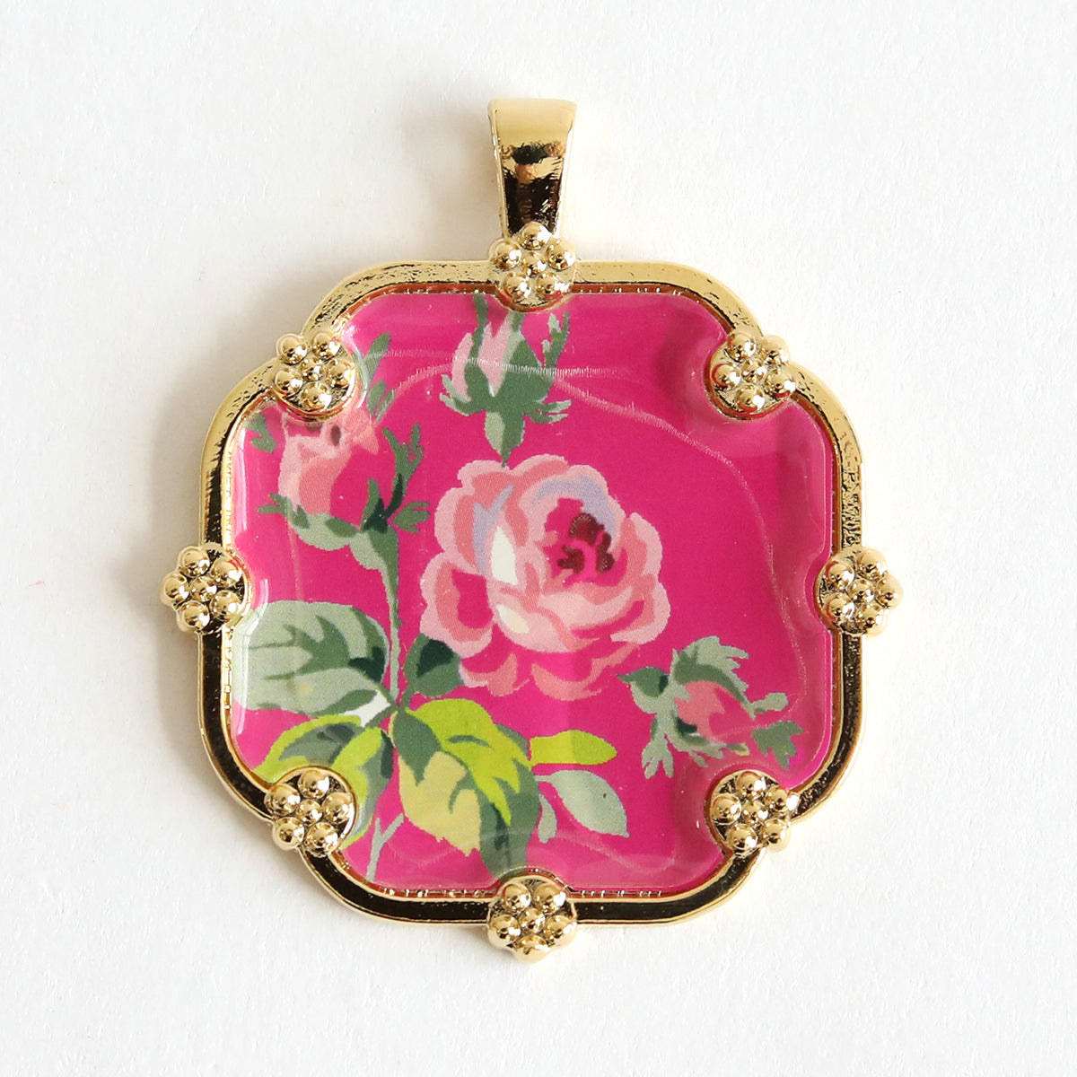 A decorative pendant from the Set of 2 Gold Necklaces Kit, featuring a gold frame and a pink floral design with a rose and green leaves on a pink background, perfect for making statement necklaces.