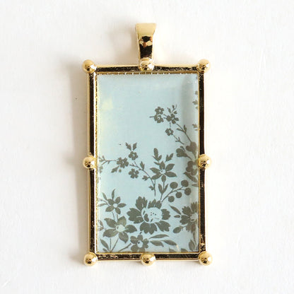 Make a bold statement with the Set of 2 Gold Necklaces Kit, featuring one decorative rectangular pendant adorned with a floral design on a blue background. Perfect for those who love eye-catching jewelry.