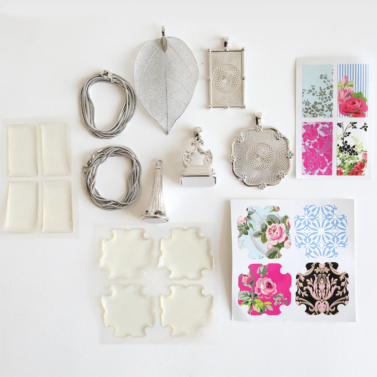 Set of 2 Silver Necklaces Kit, featuring silver-tone leaf pendants, wire, adhesive squares, and floral patterned papers on a white background. Perfect for crafting your own statement necklaces or adding unique designs to enhance a necklace kit.