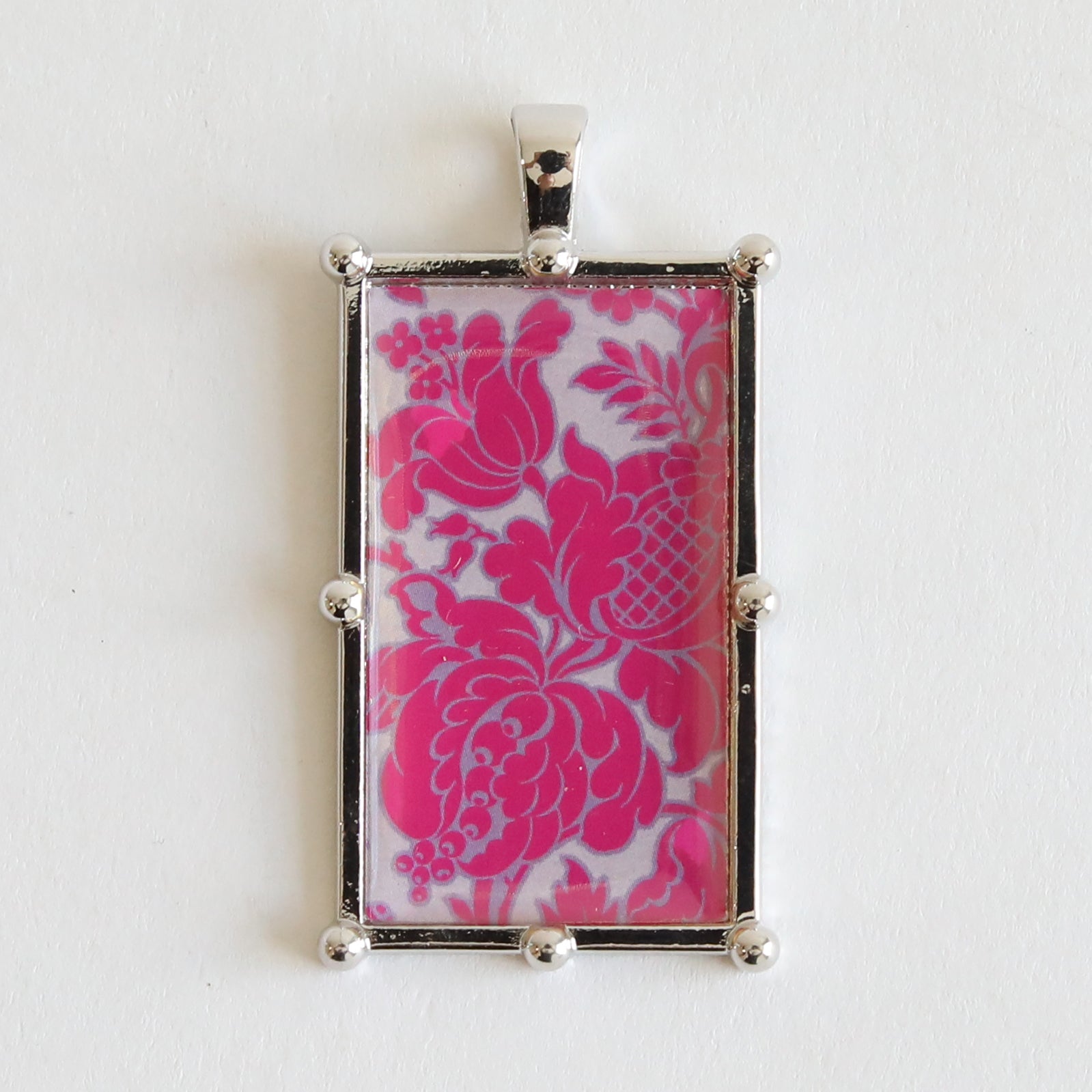 A rectangular pendant with a silver-tone metallic frame featuring a pink floral pattern on a white background, ideal for enhancing the Set of 2 Silver Necklaces Kit or crafting unique statement necklaces.