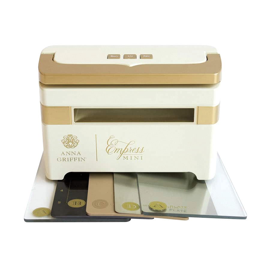 A white and gold mini die cutting and embossing machine called "Black Friday Empress Mini Bundle" by Anna Griffin, featuring the Empress Mini label, comes with accompanying plates and Festive Flourish Dies displayed in front.