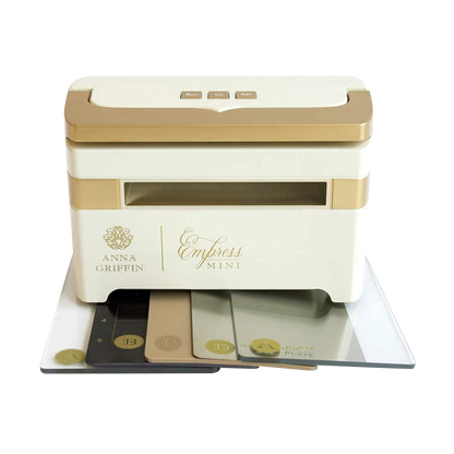 A white and gold mini die cutting and embossing machine called "Black Friday Empress Mini Bundle" by Anna Griffin, featuring the Empress Mini label, comes with accompanying plates and Festive Flourish Dies displayed in front.