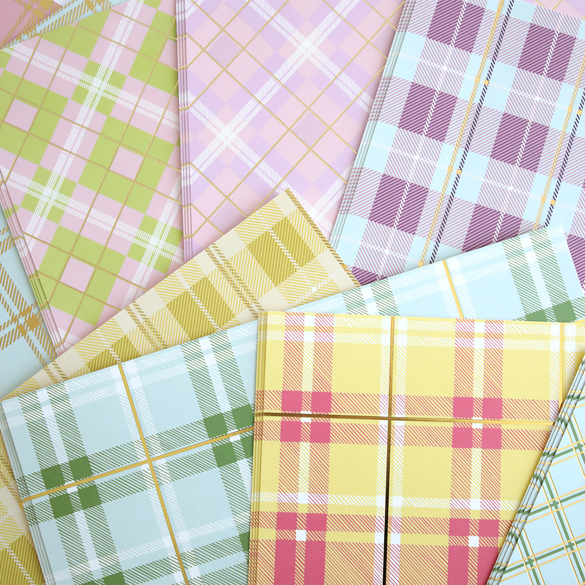 The Pastel Plaid 12x12 Cardstock set, arranged in a fan shape, showcases soft pastel hues of green, pink, yellow, and blue. Gold foil accents enhance the delicate plaid grid design, creating stunning visual harmony.