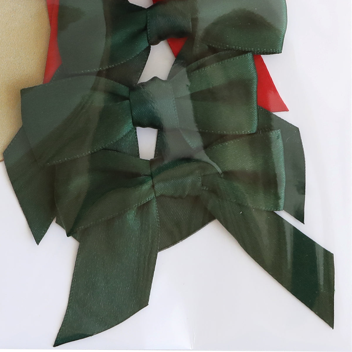 Three Medium Pre-Tied Christmas Bows in dark green satin are arranged vertically on a white background, partially covered by a clear plastic sheet.