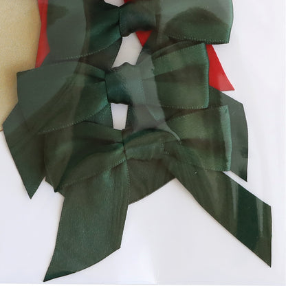 Three Medium Pre-Tied Christmas Bows in dark green satin are arranged vertically on a white background, partially covered by a clear plastic sheet.