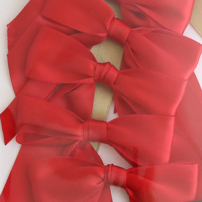Four Medium Pre-Tied Christmas Bows in red and gold are arranged vertically with overlapping layers, featuring a shimmering gold ribbon in the background.