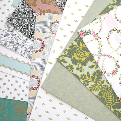 The Classic 12x12 Cardstock features a variety of sheets with floral, geometric, and abstract designs laid out overlapping each other. The colors include green, brown, and white tones, making them perfect for scrapbooks.