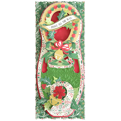 Festive holiday card with a "Jingle All The Way" message and decorative elements featuring holly, ribbons, and ornaments on a green and red background, perfect for adding to your Paper Elf Shoe Finishing School Craft Box or pairing with your Paper Elf Shoes project.